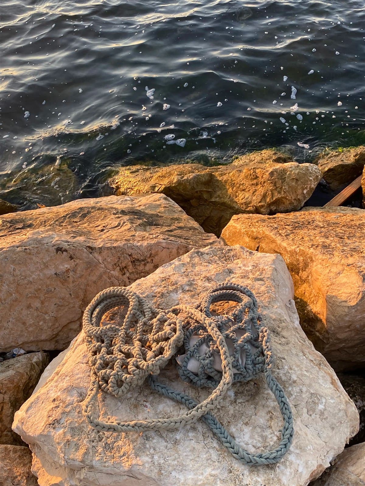 Yarn and a crochet hook resting on seaside rocks